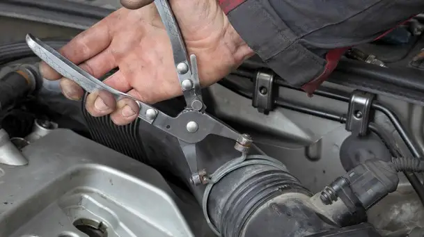 mechanic fixing hose clamp with pliers tool at car engine