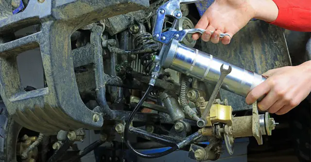 using grease gun to lubricate suspension joints on a quad bike